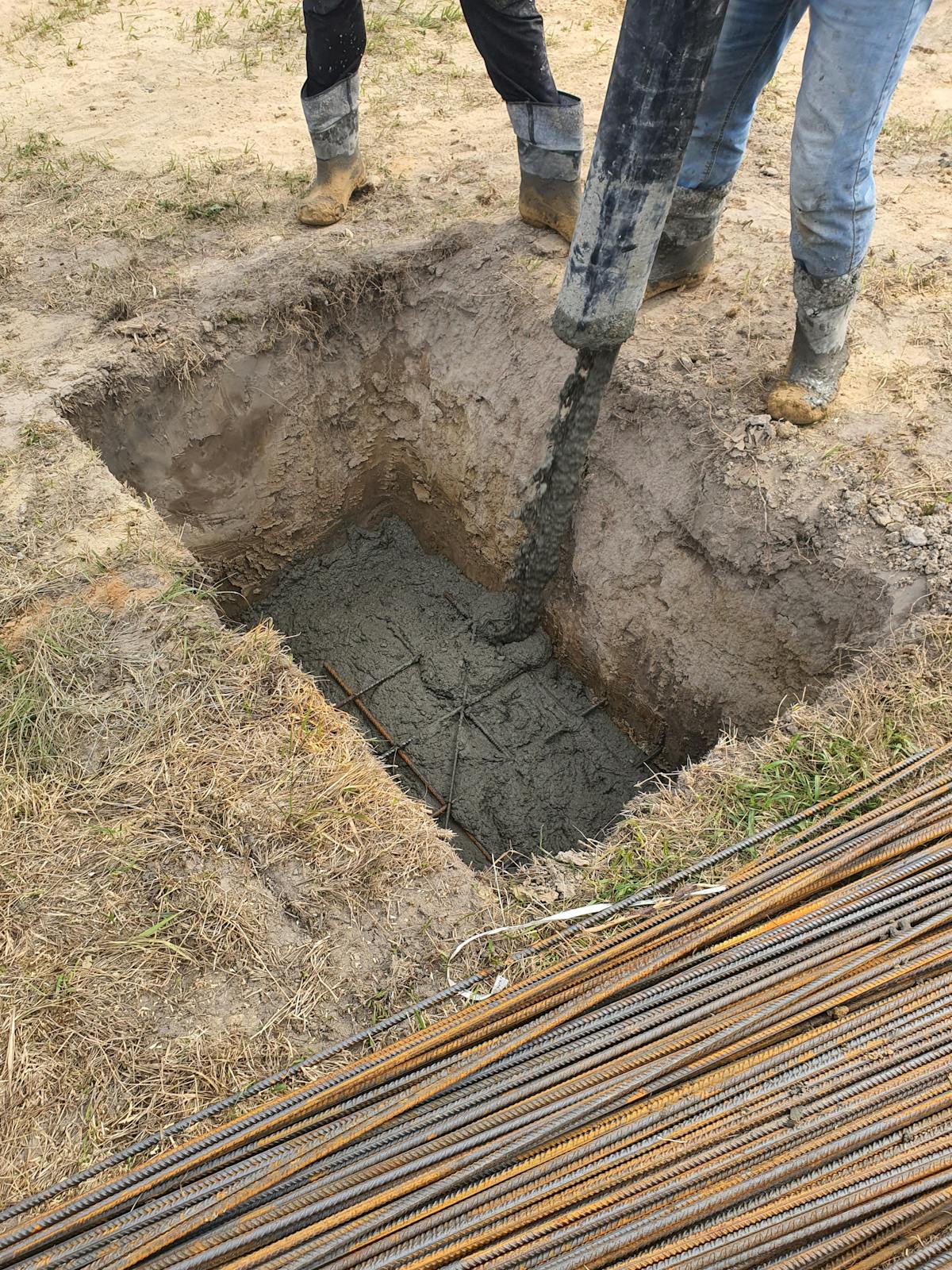 Builder filling a post hole with concrete to anchor a freshly set fence post